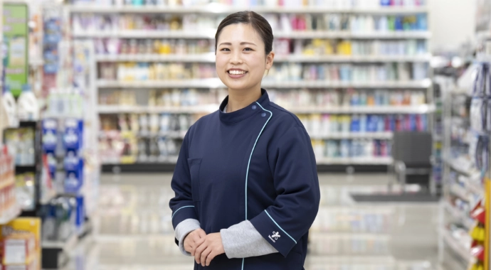 インタビューキービジュアル。Iさんが正面を向いて笑顔で立っている様子。背後は店内の開けた通路。