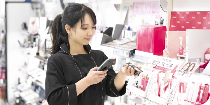 化粧品売り場にいる従業員が端末で商品を読み取って、使用期限等を調べている様子